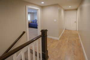Hall with an upstairs landing, light wood-style flooring, and recessed lighting