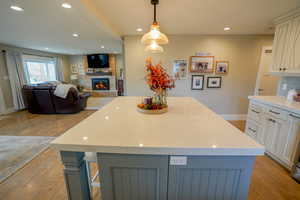 Kitchen with light wood-type flooring, pendant lighting, a center island, light stone counters, and recessed lighting