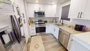 Kitchen featuring stainless steel appliances, white cabinetry, light wood-style flooring, light stone countertops, and recessed lighting