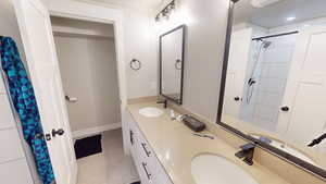 Full bath with curtained shower, double vanity, and light tile patterned floors