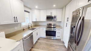 Kitchen with stainless steel appliances, white cabinetry, light wood-type flooring, recessed lighting, and light stone counters
