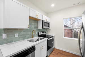 Kitchen with appliances with stainless steel finishes, decorative backsplash, white cabinetry, dark wood-type flooring, and recessed lighting