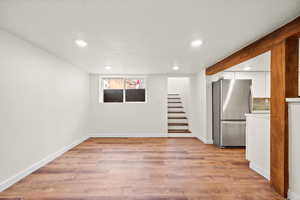 Below grade area featuring a textured ceiling, freestanding refrigerator, light wood-style flooring, stairs, and recessed lighting