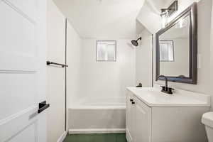 Full bath with a textured ceiling, vanity, tub / shower combination, and dark tile patterned flooring