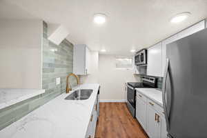 Kitchen featuring appliances with stainless steel finishes, backsplash, light stone countertops, and a textured ceiling