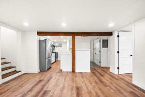 Unfurnished living room featuring recessed lighting, light wood-type flooring, electric panel, and stairs