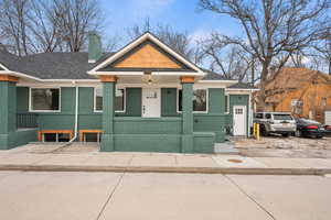View of front facade featuring brick siding, a chimney, a porch, and roof with shingles