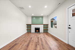 Unfurnished living room with wood finished floors, a warm lit fireplace, and recessed lighting