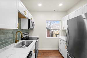 Kitchen featuring stainless steel appliances, dark wood-style flooring, light stone countertops, white cabinets, and decorative backsplash
