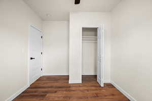 Unfurnished bedroom with dark wood-style floors, a closet, and a ceiling fan