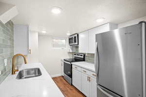 Kitchen with appliances with stainless steel finishes, white cabinetry, backsplash, dark wood finished floors, and a textured ceiling