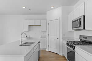 Kitchen featuring stainless steel appliances, white cabinets, light wood-type flooring, recessed lighting, and a kitchen island with sink