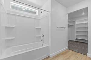 Full bath featuring light wood-style flooring, tub / shower combination, and a walk in closet