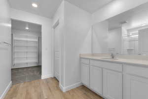 Bathroom featuring a textured ceiling, a spacious closet, vanity, light wood-style flooring, and recessed lighting