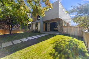 Rear view of property featuring a fenced backyard, stone siding, a balcony, and a patio area