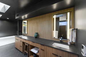 Bathroom with double vanity, a skylight, and wood walls