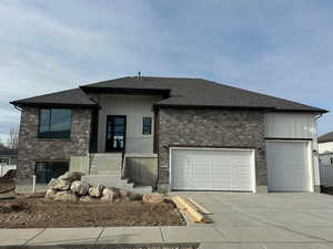 View of front facade featuring stone siding, roof with shingles, driveway, and a porch