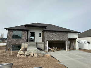 View of front of house featuring stone siding, driveway, a shingled roof, and a patio area