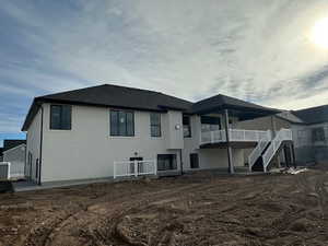 Back of property featuring a patio, stairway, stucco siding, and roof with shingles