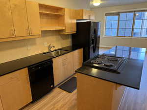 Kitchen featuring open shelves, light wood finished floors, backsplash, black appliances, and dark stone countertops