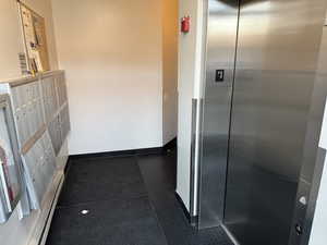 Hall featuring elevator, mail area, tile patterned floors, and a baseboard heating unit