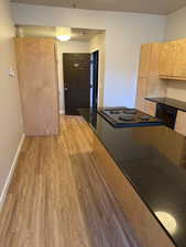 Kitchen with light wood finished floors, light brown cabinets, black appliances, and dark stone counters