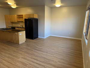 Kitchen with dark countertops, black fridge with ice dispenser, open shelves, and light wood-style flooring