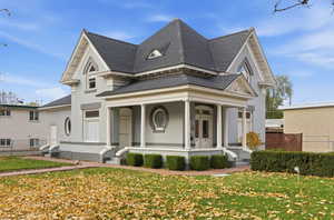 View of front facade with roof with shingles, a front yard, and a porch
