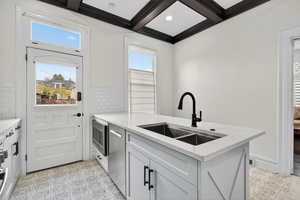 Kitchen with a peninsula, light stone countertops, appliances with stainless steel finishes, beam ceiling, and coffered ceiling