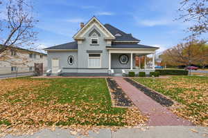 View of front facade featuring covered porch, a chimney, brick siding, and a shingled roof