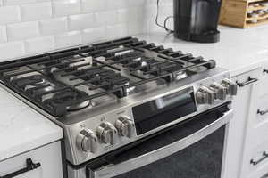 Kitchen view of light stone countertops, white cabinetry, stainless steel gas range oven, and backsplash