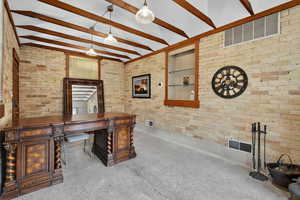 Office space featuring brick wall, beamed ceiling, and built in shelves