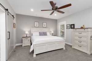Master bedroom featuring a barn door, light carpet, recessed lighting, and a ceiling fan.