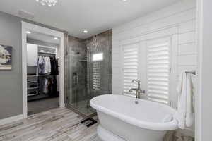 Bathroom with a walk in closet, a freestanding bath, a stall shower, recessed lighting, and light wood-style floors