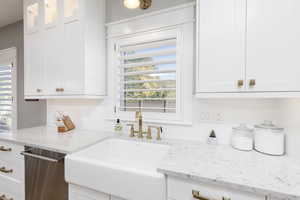 Kitchen featuring white cabinetry, backsplash, light stone countertops, and classic sink.