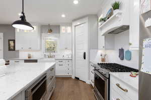 Kitchen with appliances with stainless steel finishes, white cabinets, pendant lighting, light stone countertops, and dark wood flooring.