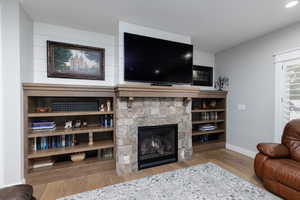 Living area featuring a stone fireplace and light wood-style flooring, and built in bookcases.