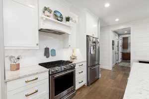 Kitchen with stainless steel appliances, white cabinetry, dark wood-style floors, recessed lighting, and light stone countertops.
