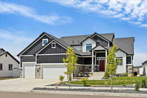 Craftsman-style home featuring stone siding, driveway, a shingled roof, and a garage