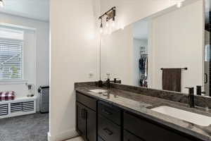 Full bathroom with plenty of natural light, double vanity, a spacious closet, and dark carpet