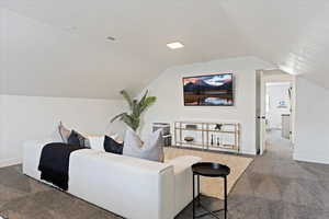 Carpeted home theater room with vaulted ceiling and baseboards
