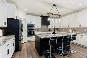 Kitchen with decorative light fixtures, dark cabinetry, white cabinets, a kitchen bar, and stainless steel appliances