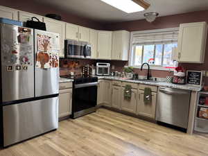Kitchen with appliances with stainless steel finishes, light wood-style floors, and light stone countertops