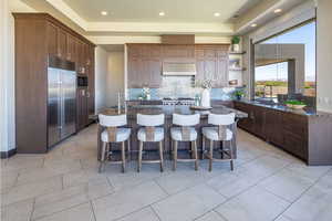 Kitchen with a kitchen island with sink, decorative backsplash, open shelves, built in refrigerator, and dark stone countertops