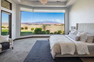 Carpeted bedroom with a tray ceiling, multiple windows, and access to exterior