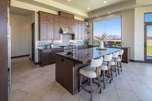 Kitchen featuring backsplash, a kitchen island with sink, dark stone countertops, a kitchen bar, and open shelves