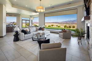 Tiled living room with a raised ceiling, a stone fireplace, a chandelier, and recessed lighting