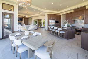 Dining room with a tray ceiling, a chandelier, recessed lighting, a fireplace, and light tile patterned floors