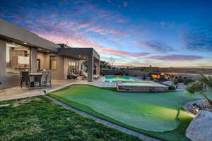Yard at dusk featuring a putting area, a patio area, a fenced backyard, and a pool with connected hot tub