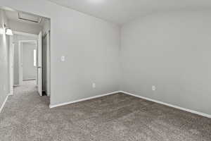Unfurnished room with carpet floors, a textured ceiling, attic access, and lofted ceiling